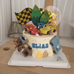 Cars racing theme birthday cake with toy car toppers, chocolate soil crumble, checkered flag decoration and custom name on cake