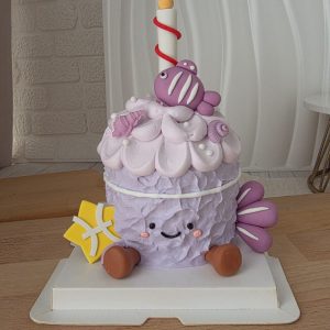 Pisces Horoscope Jellycat Style Birthday Cake with pastel purple textured cream, cute smiling face, fondant fish decorations, seashell accents, candle topper, and Pisces zodiac symbol by The Cake Alchemy Puchong Selangor