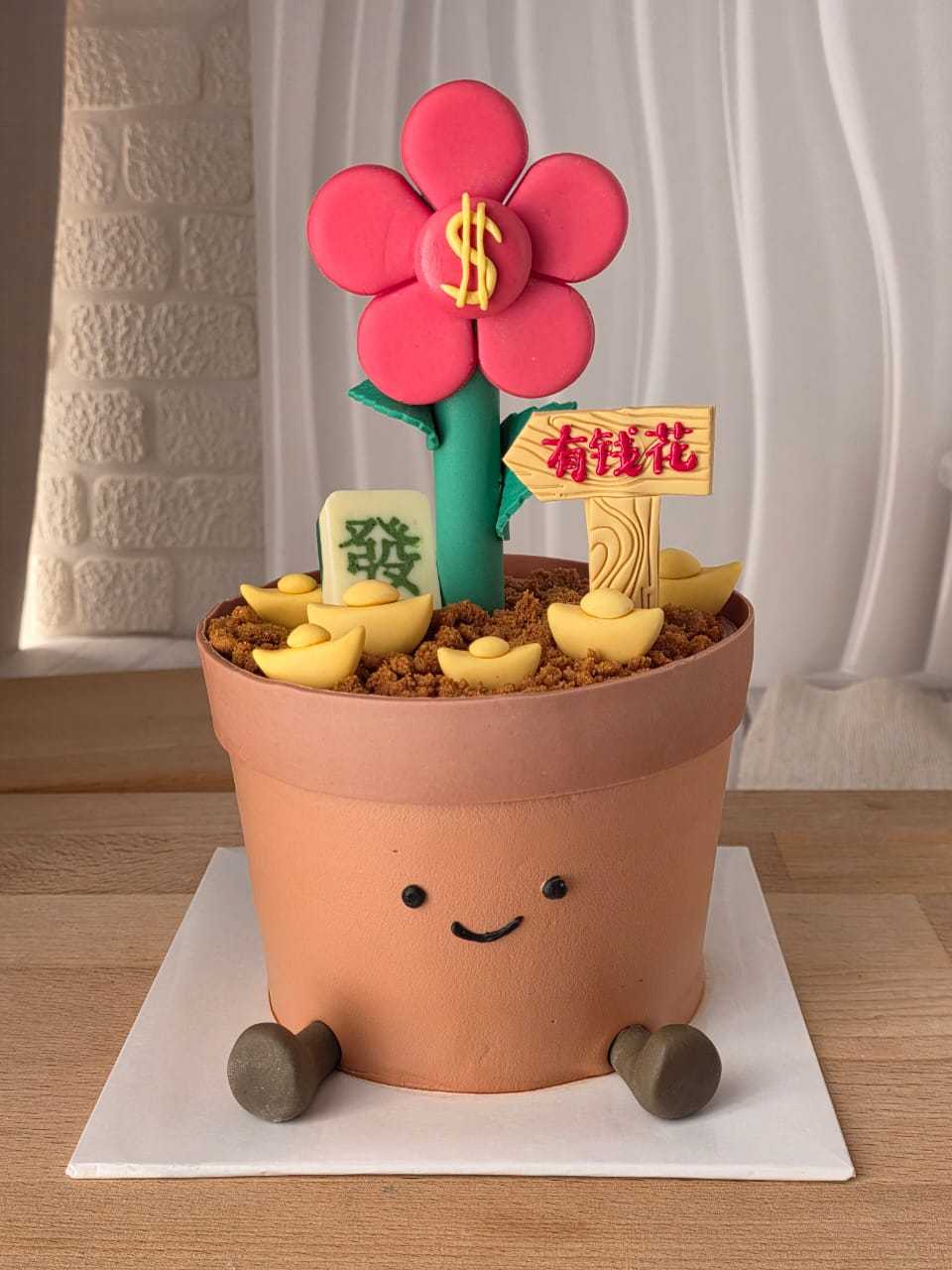 Jellycat-style flower pot cake with a smiling face, money flower topper, gold ingots, and prosperity-themed decorations by The Cake Alchemy in Puchong Selangor Malaysia.