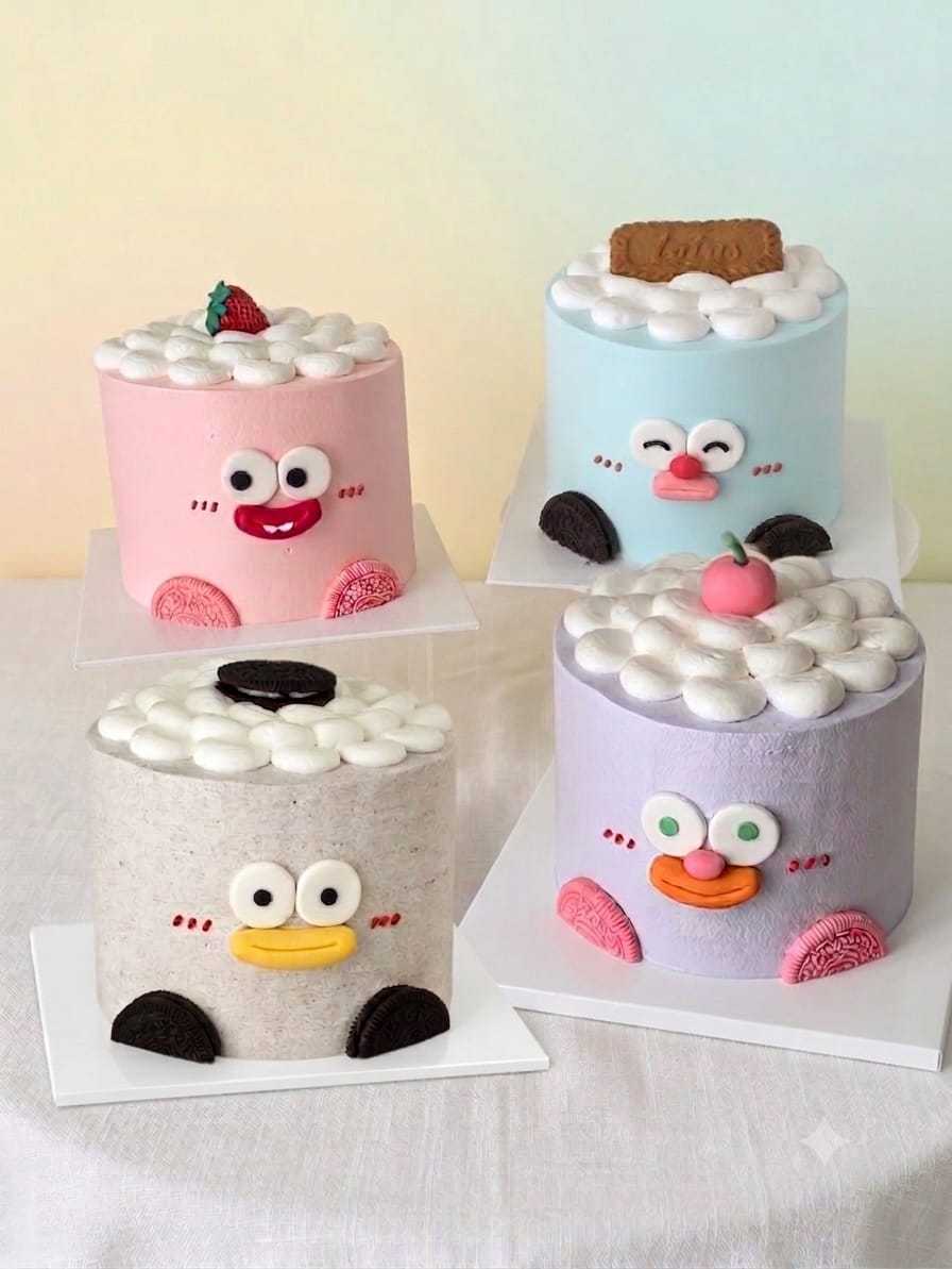 Collection of ugly-cute character cakes in pastel colors featuring playful cartoon faces, fluffy cream dollops, cookies, strawberries, and whimsical decorations by The Cake Alchemy.