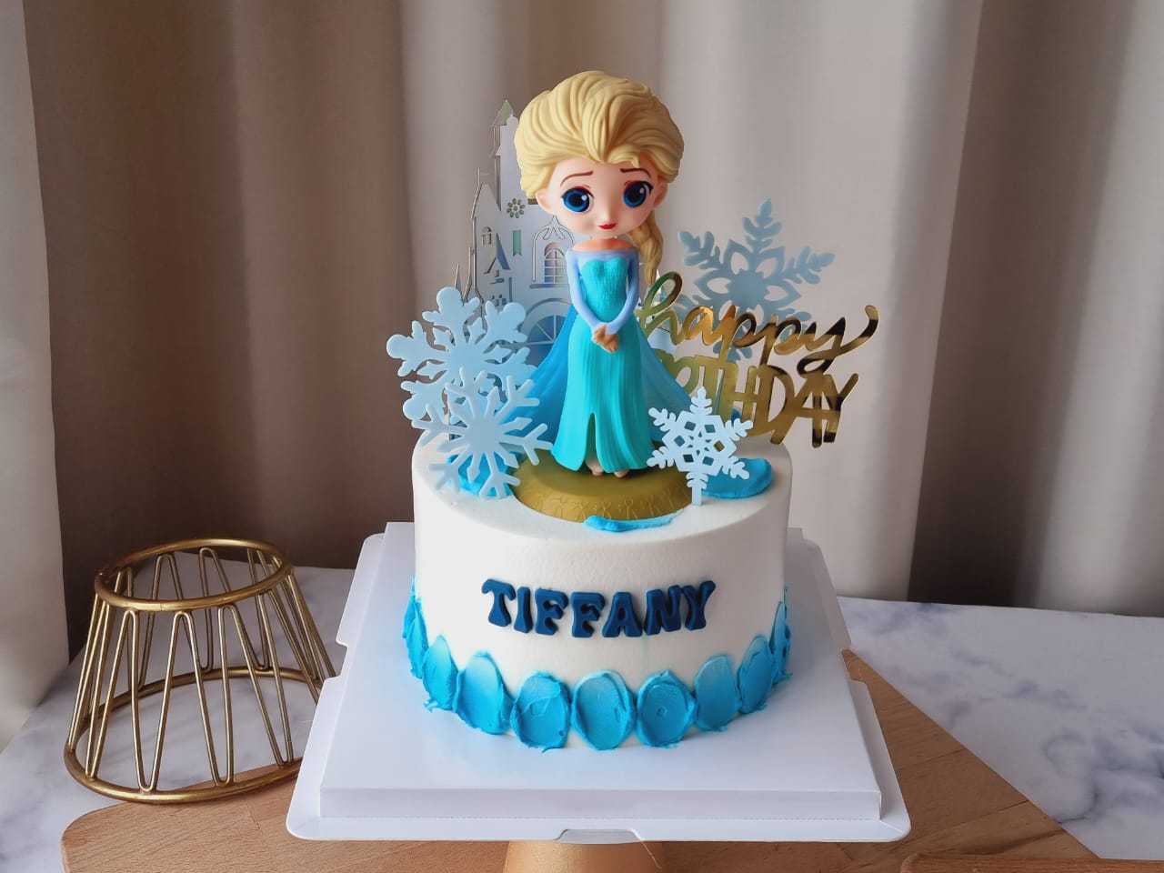 Elsa Frozen birthday cake with princess topper, snowflakes, castle decorations, blue cream accents, and personalized name by The Cake Alchemy in Puchong Selangor Malaysia.