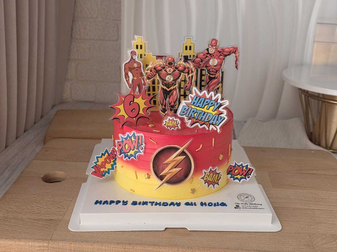 The Flash superhero birthday cake with comic-style toppers, red and yellow cream, city skyline backdrop, and personalized birthday message by The Cake Alchemy in Puchong Selangor Malaysia.