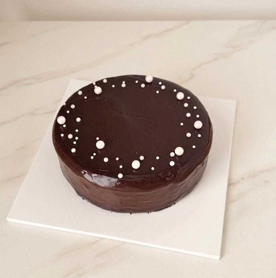 New York cheesecake with glossy chocolate glaze and elegant white pearl decorations by The Cake Alchemy