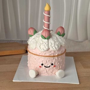 Peach Jellycat style birthday cake with cute smiling face, peach decorations, fluffy cream, and candle centerpiece by The Cake Alchemy