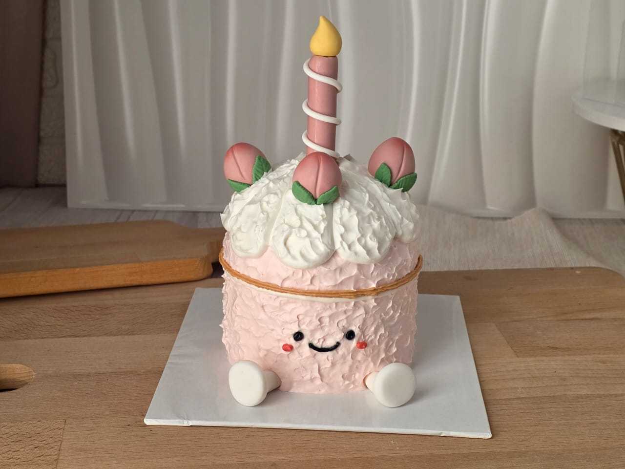 Peach Jellycat style birthday cake with cute smiling face, peach decorations, fluffy cream, and candle centerpiece by The Cake Alchemy