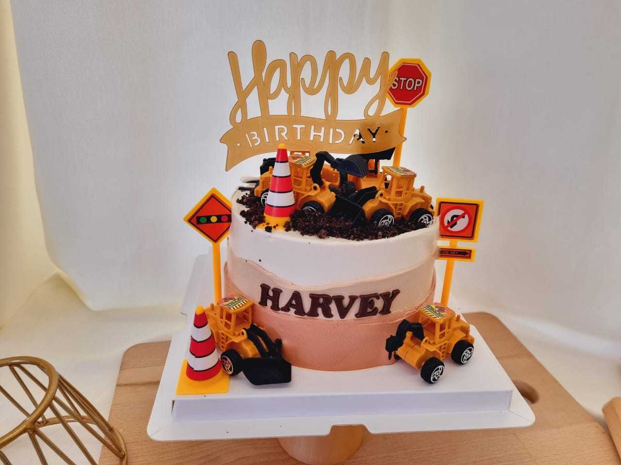 Construction theme birthday cake with excavator toys, construction trucks, traffic signs, cookie rocks, and personalized name by The Cake Alchemy