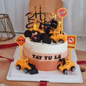Construction theme birthday cake with excavator toys, construction trucks, traffic signs, cookie rocks, and personalized name by The Cake Alchemy