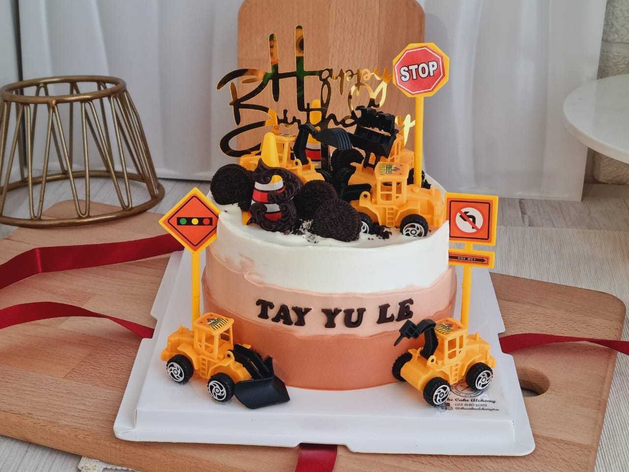 Construction theme birthday cake with excavator toys, construction trucks, traffic signs, cookie rocks, and personalized name by The Cake Alchemy